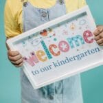 Dziecko trzyma kolorowy plakat welcome to kindergarten na turkusowym tle