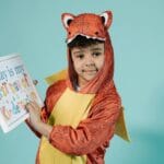 Dziecko w stroju dinozaura trzyma tabliczkę z napisem pierwszy dzień w przedszko