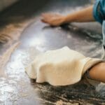 Kucharz w niebieskiej koszuli zagniata ciasto na pizzę na oprószonym blacie