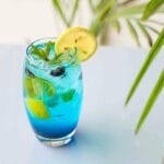 Niebieski bezalkoholowy koktajl z cytryną, miętą i jagodami na tle tropików