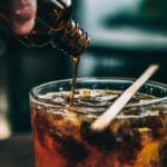 Syrop wlewający się do szklanki z mrożoną kawą i drewnianym mieszadełkiem