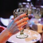 Dłoń kobiety z kieliszkiem wina przy elegancko nakrytym stole